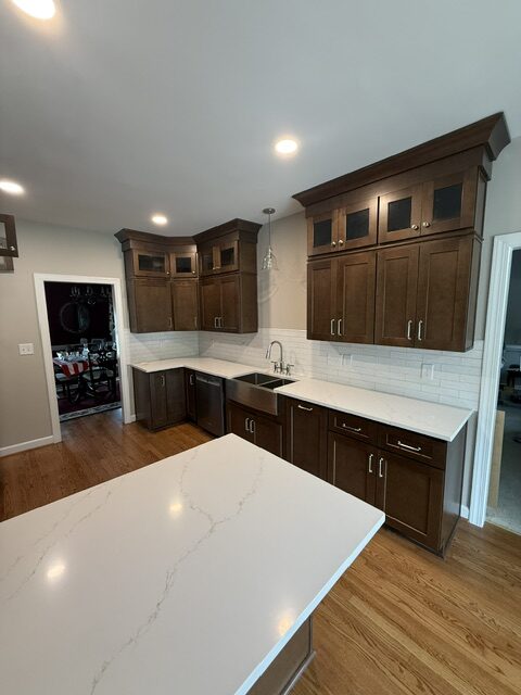Remodeled kitchen with dark wood cabinets, white countertops, farmhouse sink, and large peninsula